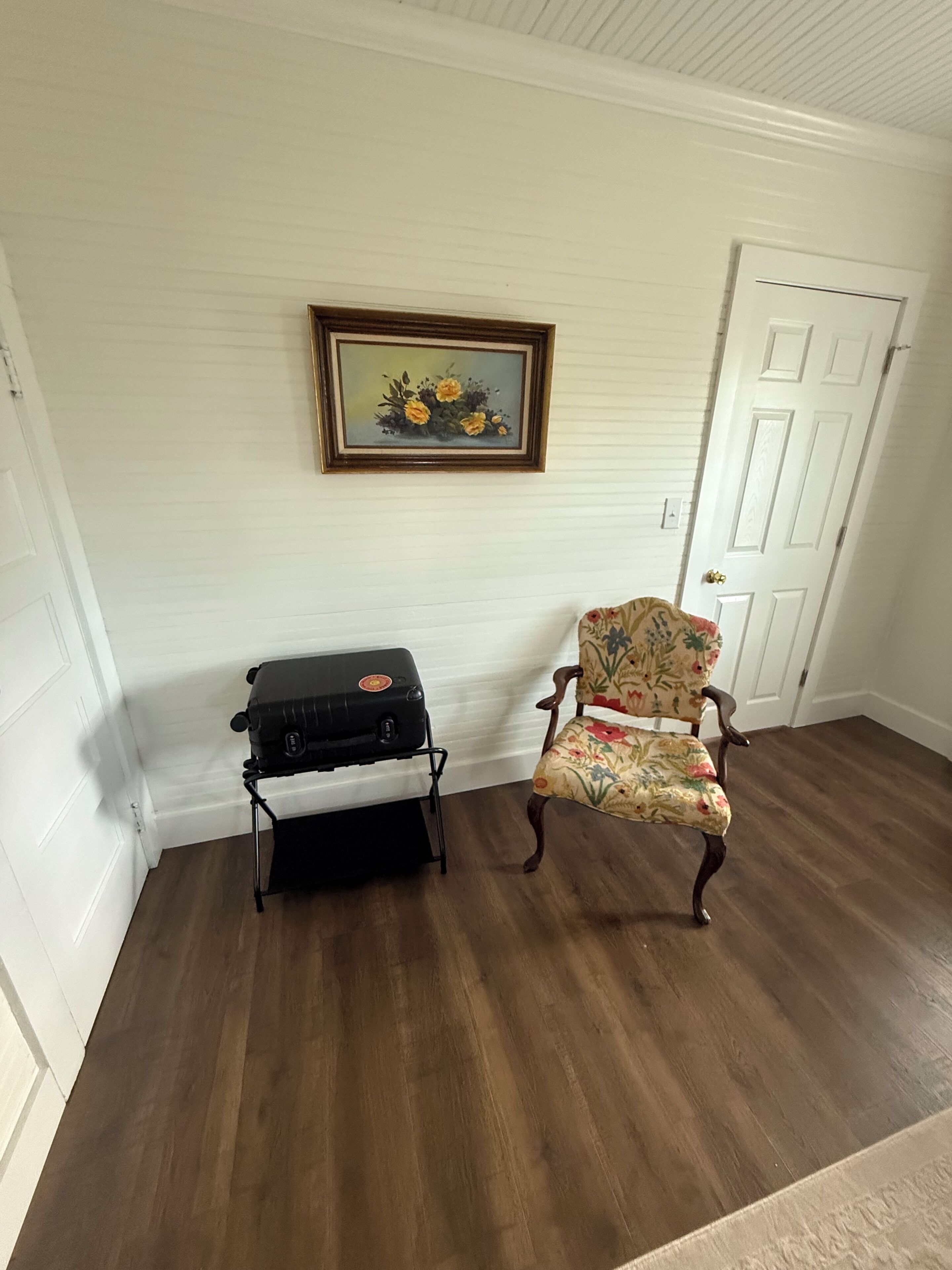 Ein Zimmer mit Holzboden, einem schwarzen Grill, einem floralen Sessel und einem gerahmten Gemälde an der Wand.