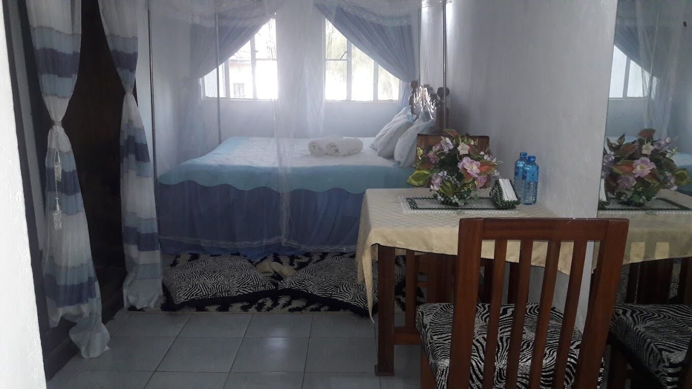 A bedroom with a bed, a table with a vase of flowers, and a chair.