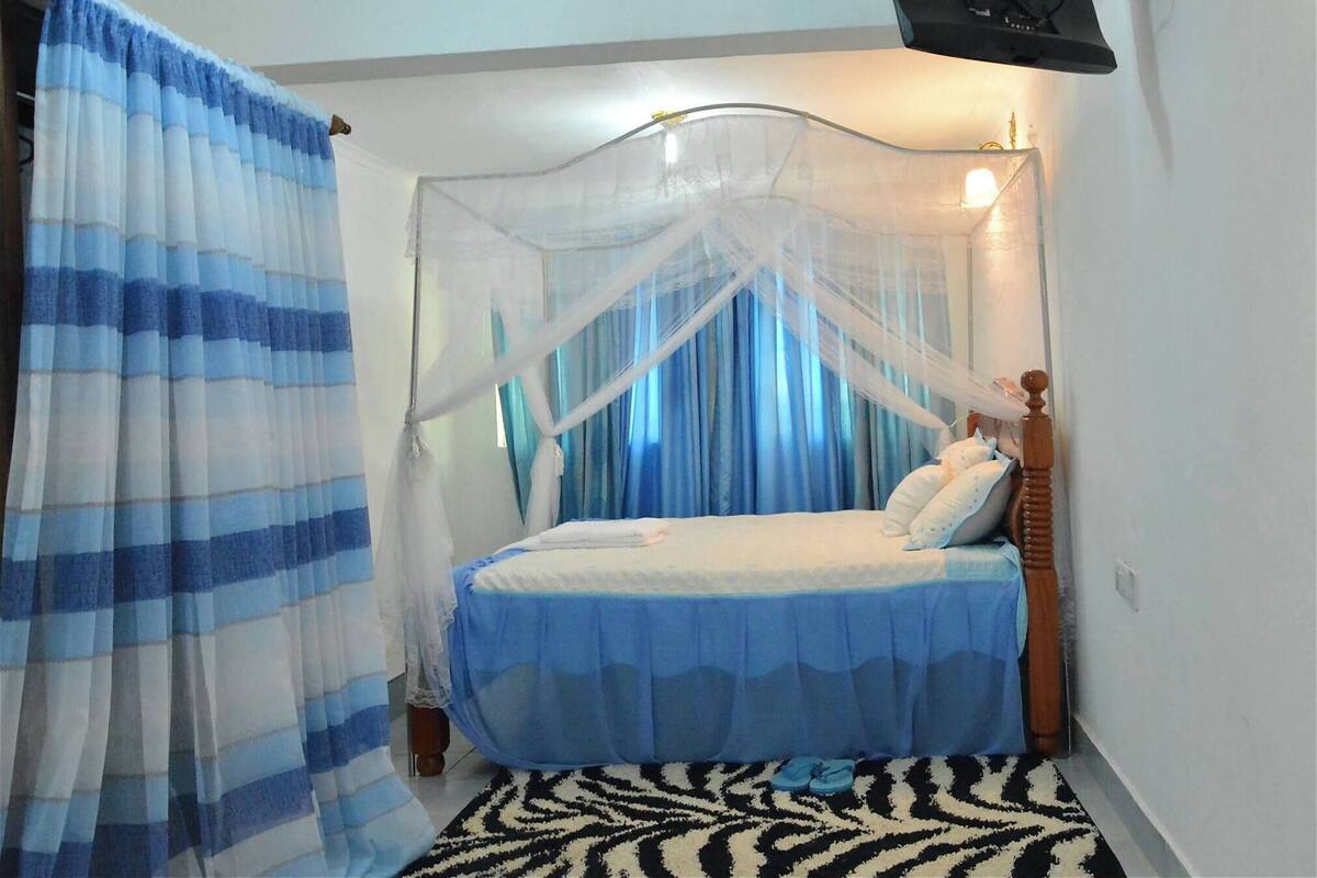 A bedroom with a bed, a mosquito net, and a nightstand.