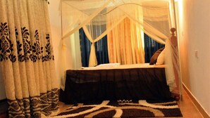 Quarto com cama, cortinas, dossel, tapete e mesa de cabeceira.