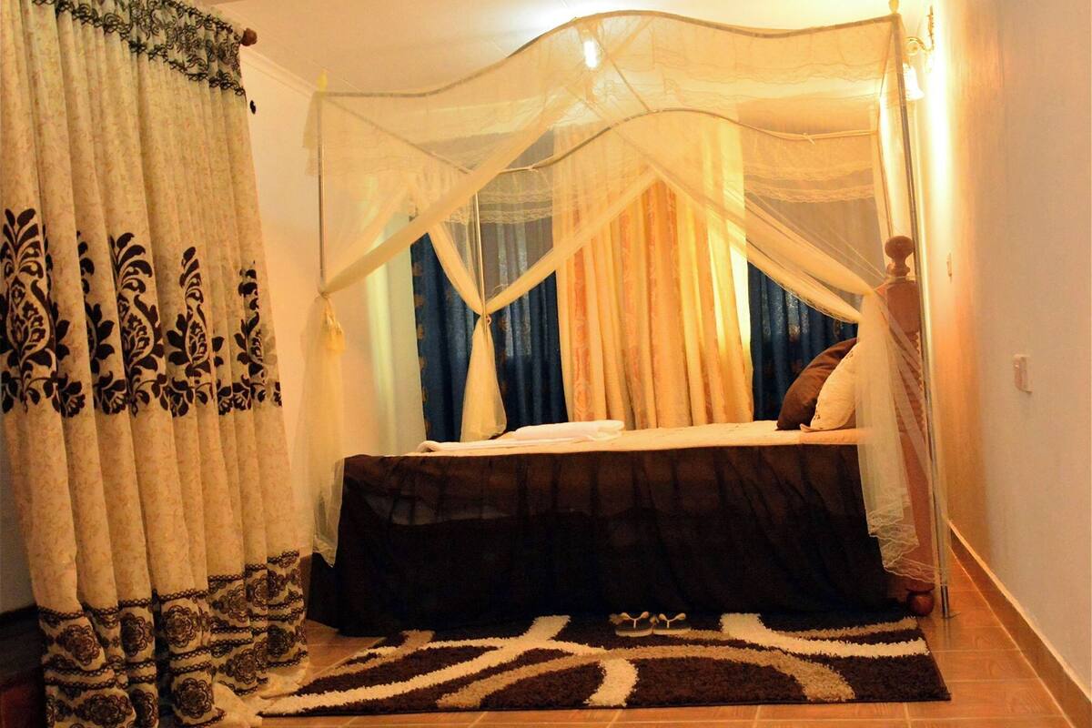 A bedroom with a bed, curtains, a canopy, a rug, and a nightstand.