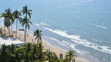 A beach with palm trees, a boat on the sand, and a clear view of the ocean.