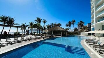 A swimming pool with lounge chairs and palm trees, surrounded by modern buildings.