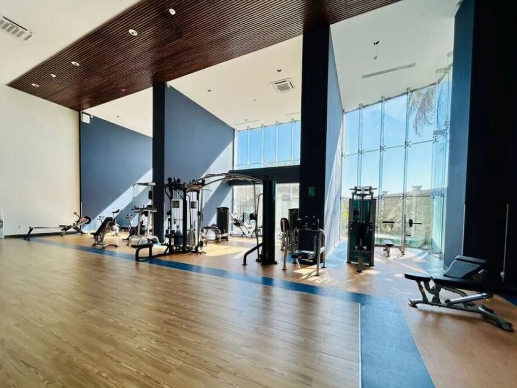 A gym with exercise equipment, large windows, and a wooden floor.