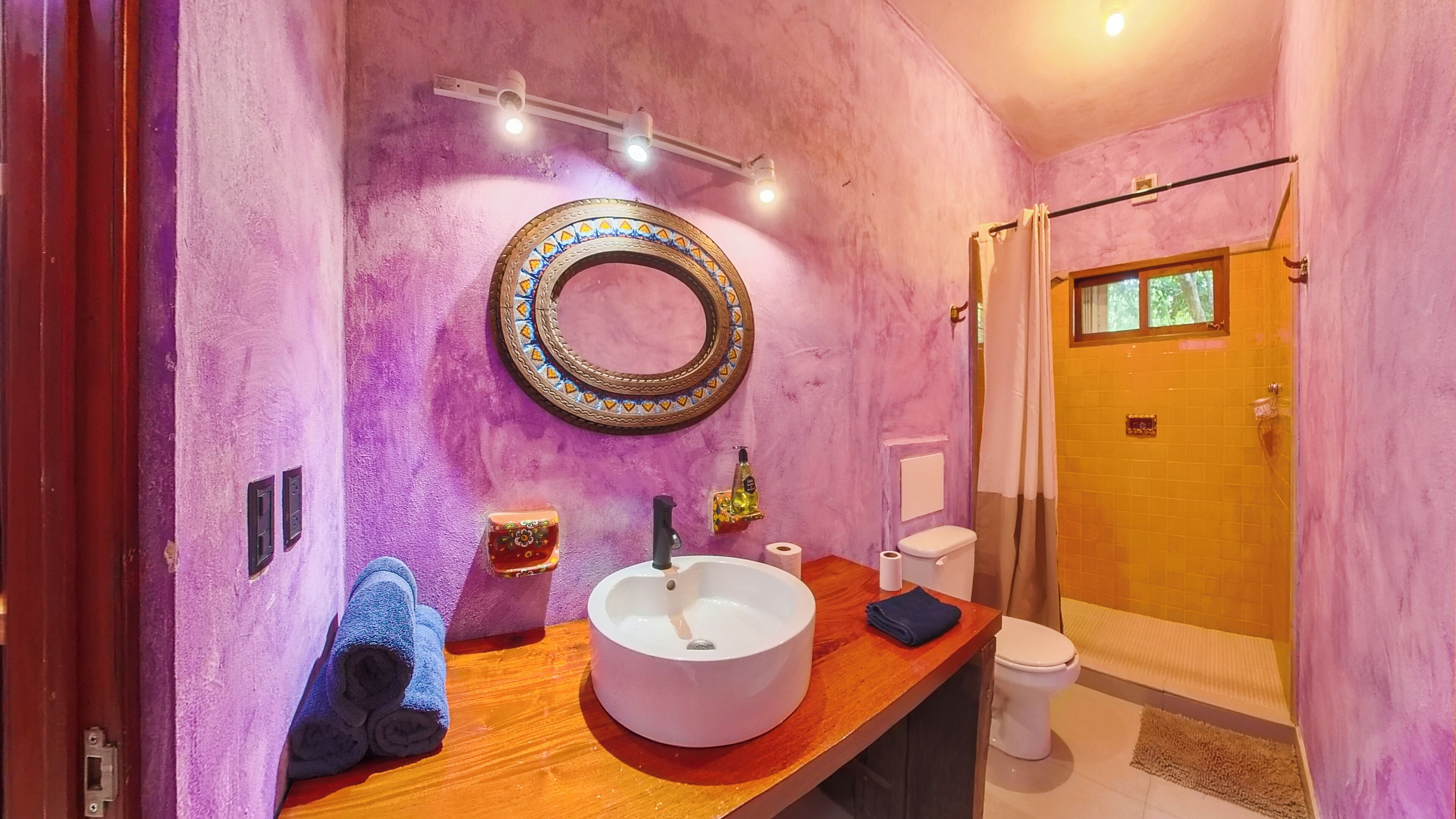 A bathroom with a round mirror, a sink, a toilet, and a shower area.