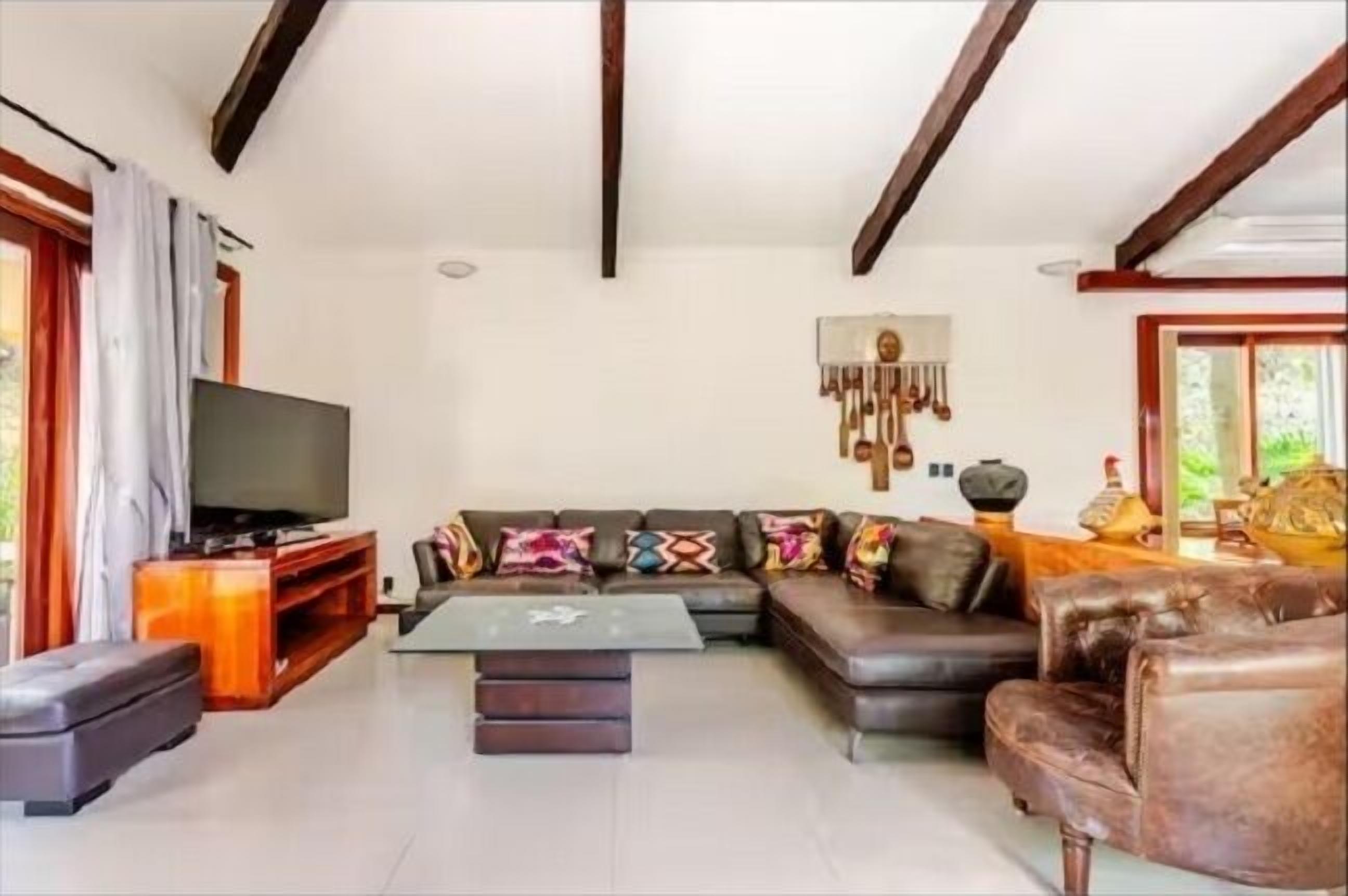 Una sala de estar con sofá, reposapiés, mesa de centro, televisor y un tapiz decorativo.
