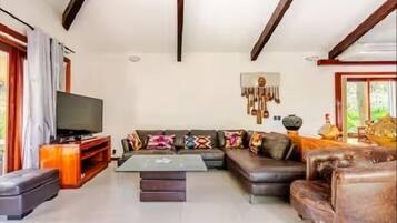 Una sala de estar con sofá, reposapiés, mesa de centro, televisor y un tapiz decorativo.