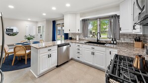 A modern kitchen with white cabinetry, a built-in dishwasher, a gas stove, and a window with curtains. - Soothing 5-bedroom house with AC in charming Willmar (Willmar)