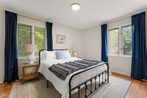 Une chambre à coucher avec un lit, des lampes de chevet, une table de chevet, une fenêtre avec des rideaux et un tableau encadré au mur.