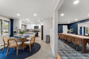 Une cuisine moderne avec des meubles blancs, un coin repas doté d’une table ronde et de chaises, ainsi qu’une longue table à manger avec des chaises.