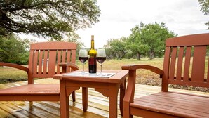 Eine Holzterrasse mit einem Tisch und zwei Stühlen, einer Weinflasche und zwei Gläsern auf dem Tisch.