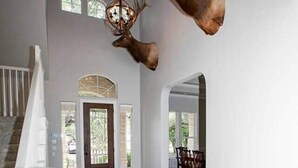 Ein geräumiges Foyer mit einer imposanten Treppe, einer Chandelüster und aufgehängten Hirschköpfen an der Wand.