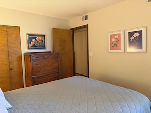A bedroom with a bed, wooden dresser, and two framed floral pictures on the wall. - Charming 1-bedroom condo in Frisco (Frisco)