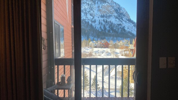 A wooden deck with a view of a snowy mountain and a row of colorful houses. - Charming 1-bedroom condo in Frisco (Frisco)