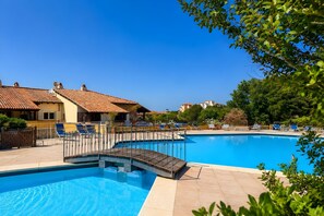 A swimming pool with a wooden deck, lounge chairs, and a building with a tiled roof.
