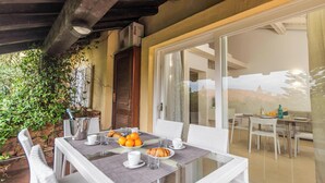 An outdoor dining area with a glass table, white wicker chairs, and a view of the landscape through a glass door. - Rotondo Dream Suite 1, Porto Rotondo, Italy (Porto Rotondo)