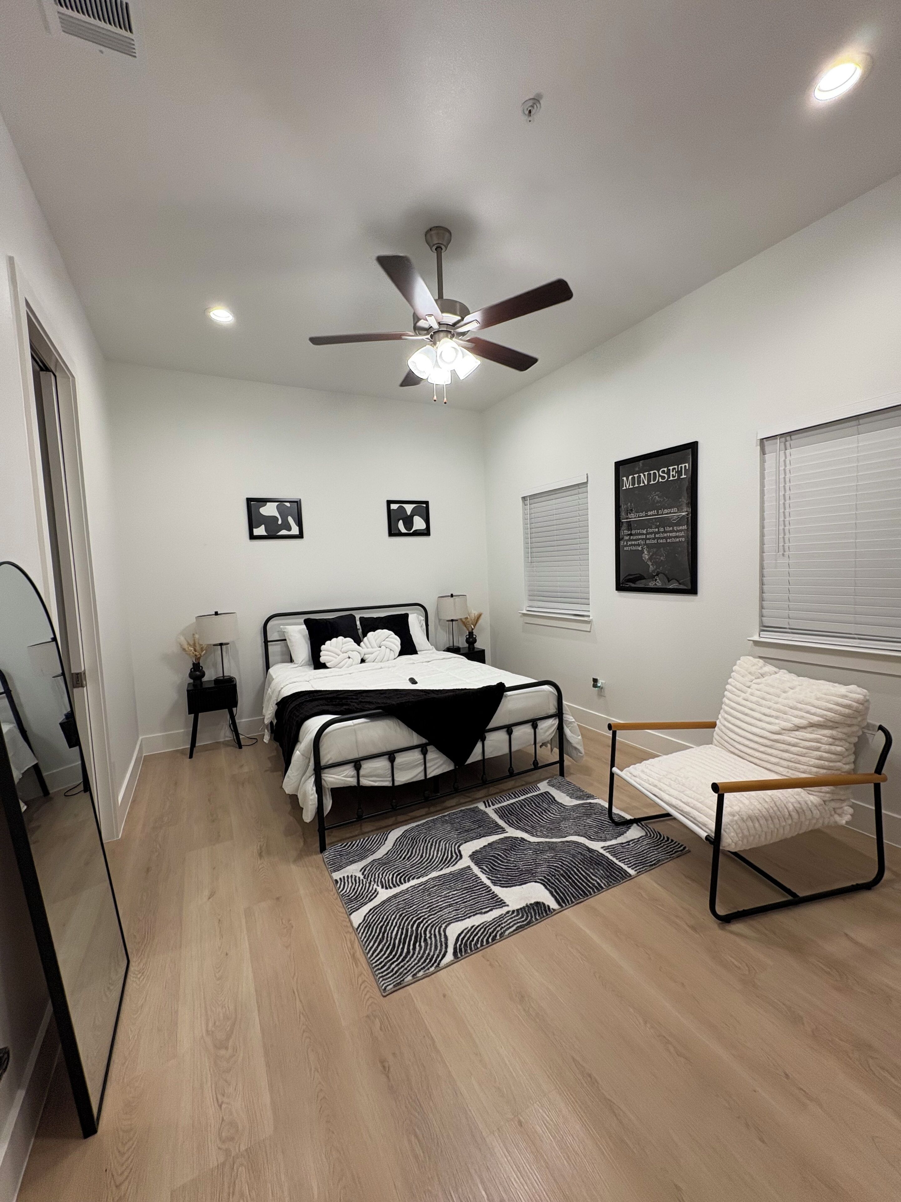 A bedroom with a bed, a chair, a ceiling fan, and a wall-mounted light fixture.