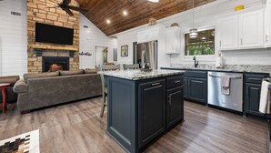 A modern kitchen with dark cabinetry, a central island, and a stone fireplace.