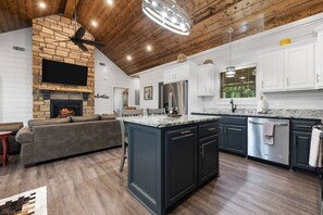 A modern kitchen with dark cabinetry, a central island, and a stone fireplace.