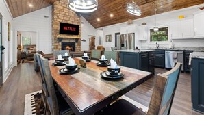 A modern kitchen with a stone fireplace, a dining area with a wooden table, and a living room with a sofa.