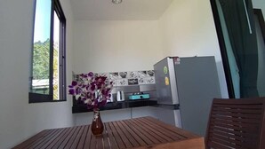 A compact kitchen with a refrigerator, a window, and a table with a vase of flowers. - Hillside Studio Vacation Apartment with Pool (Kamala, Kathu District, Phuket)