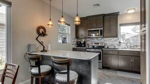 Una cocina moderna con una isla central, taburetes de bar, electrodomésticos de acero inoxidable e iluminación colgante.