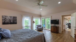 A bedroom with a large bed, a ceiling fan, a TV, and a balcony with a chair. - Peaceful Retreat w/Lakeview in Hot Springs Village (Hot Springs Village)