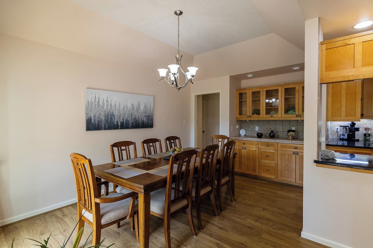 Un comedor con mesa y sillas de madera, una araña y una cocina con armarios y electrodomésticos de madera.