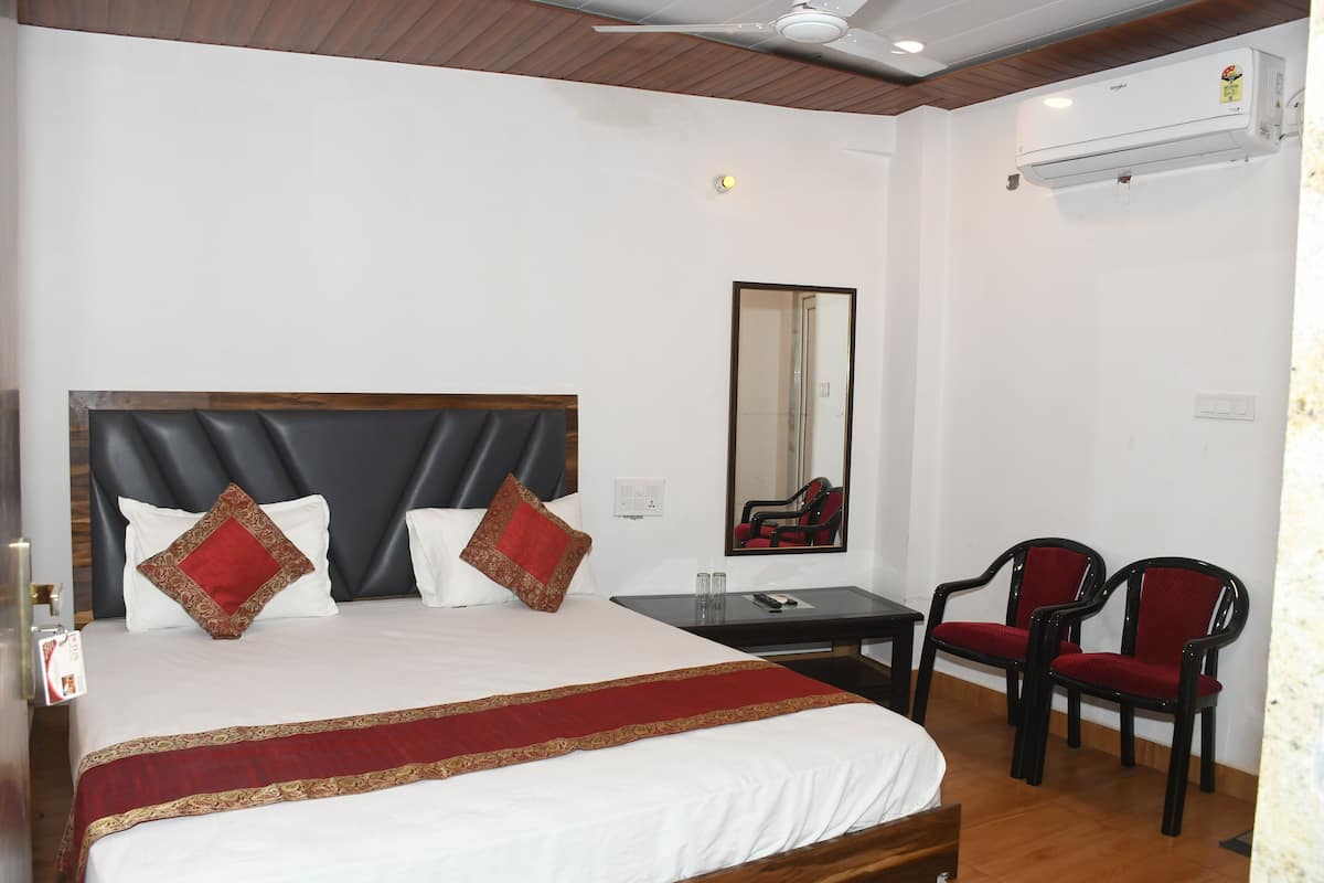 A hotel room with a large bed, a desk, two chairs, a mirror, and an air conditioning unit.