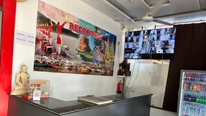A reception area with a large poster, a digital screen displaying multiple images, a statue, and a refrigerator with beverages. - Lotus Hotel Inn (Varanasi)