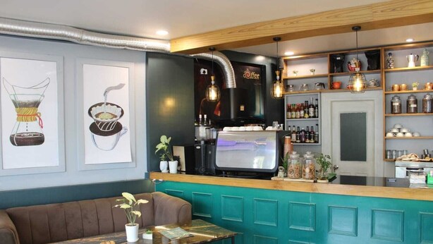A cozy bar area with a teal-colored counter, a coffee machine, and shelves with various bottles and jars. - Lotus Hotel Inn (Varanasi)