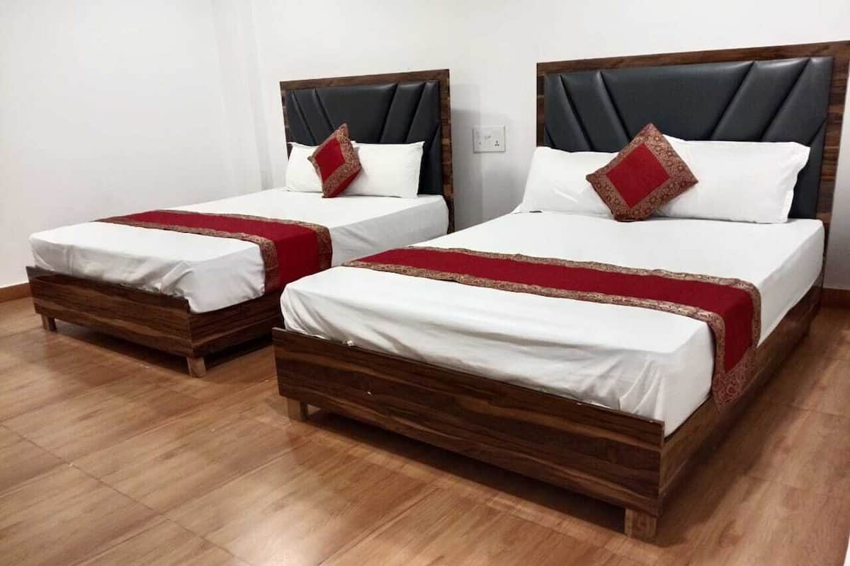 Two wooden beds with white linens and red decorative pillows in a room with wooden flooring.