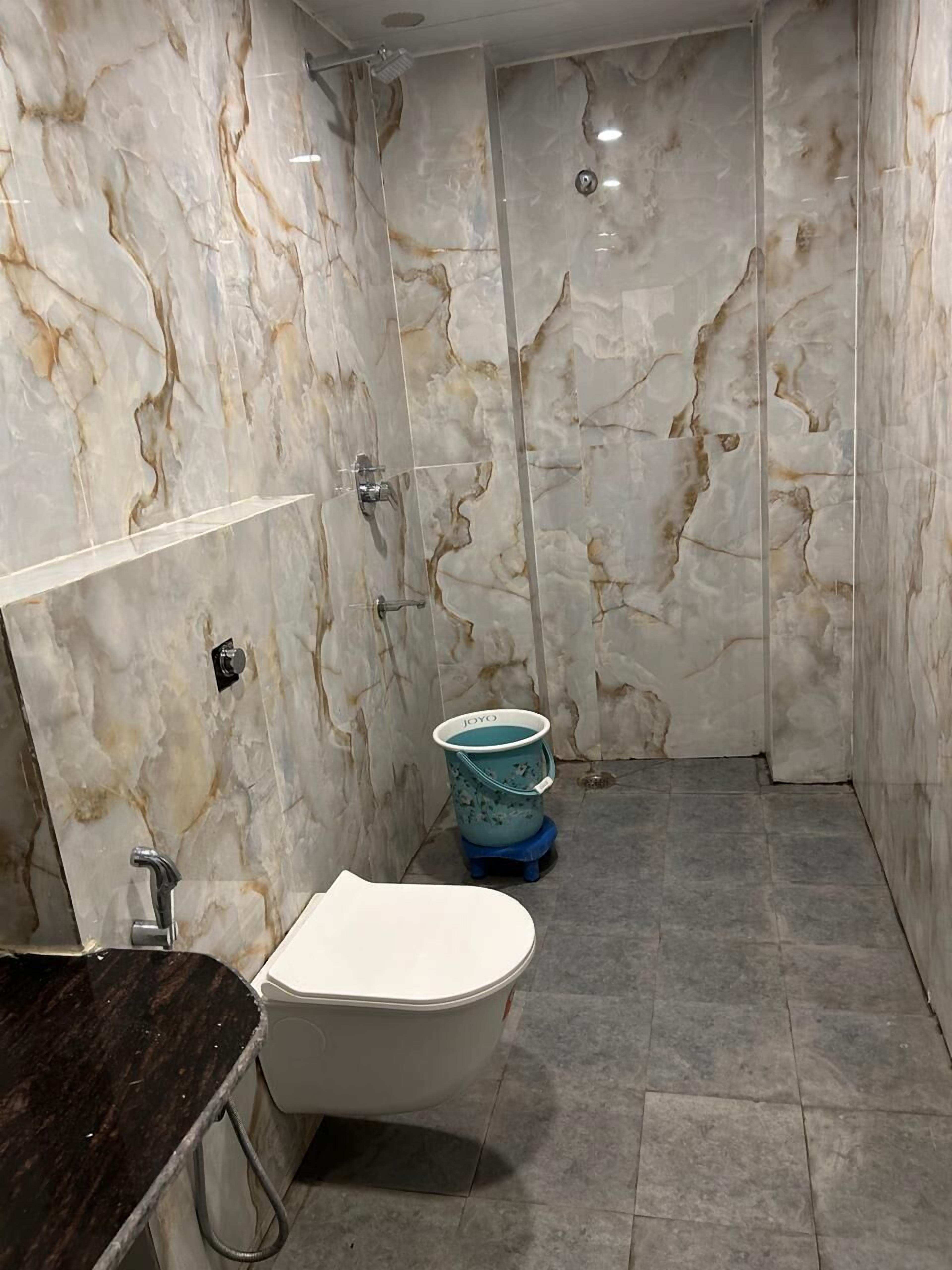 A bathroom with a marble wall, a freestanding bathtub, a toilet, and a shower area.