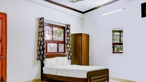 A bedroom with a bed, a wardrobe, a window with curtains, and a small picture on the wall. - Lotus Hotel Inn (Varanasi)