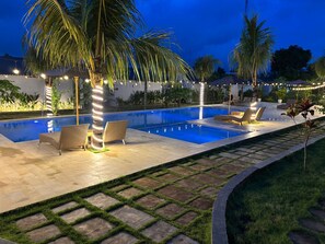 Une piscine entourée de chaises longues et de palmiers, avec une terrasse dallée et des carreaux de pierre.