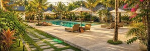 Un espace piscine aménagé avec des chaises longues, des parasols et des guirlandes lumineuses.