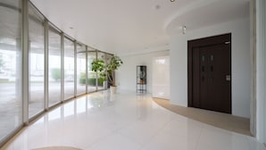 A modern, spacious lobby with large glass doors, a potted plant, a dark wooden door, and a clean, tiled floor. - lili villa hayama (Hayama)