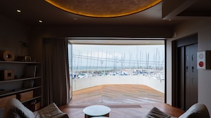 A modern interior with a curved wooden floor, a glass door leading to a marina view, and a seating area with a round table. - lili villa hayama (Hayama)