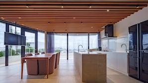 A modern kitchen with a large island, a dining area with a table and chairs, and large windows offering a view of the city. - lili villa hayama (Hayama)