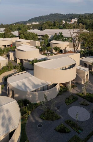 Un bâtiment moderne à l’architecture aux lignes courbes, entouré de verdure et dominé, à l’arrière-plan, par un paysage vallonné.