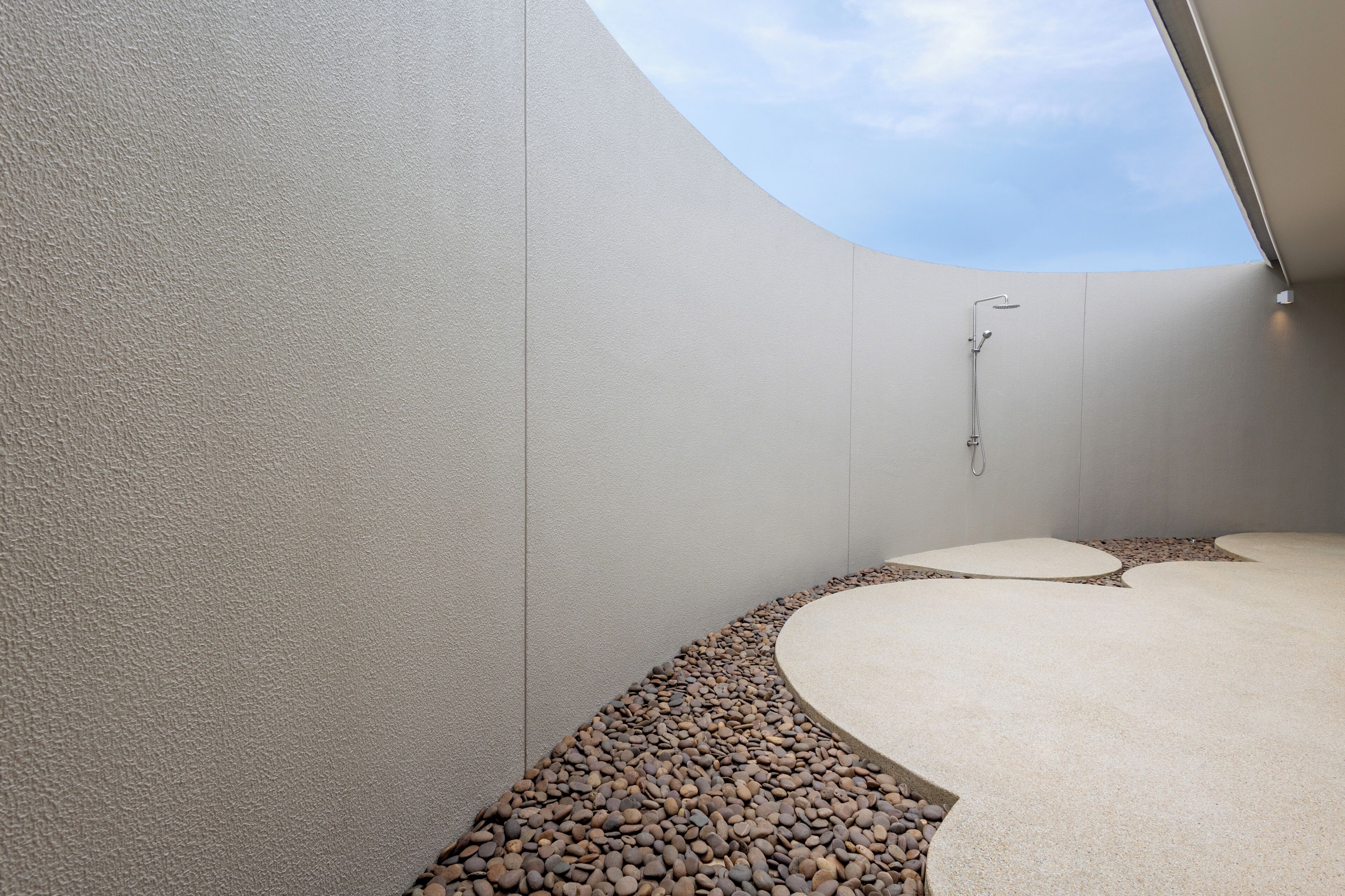 A modern bathroom with a curved ceiling, a shower area, and a pebble-patterned floor.