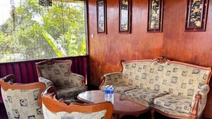 A room with a wooden wall, a ceiling fan, a round table with chairs, and framed artwork. - Audi Guest House (George Town)