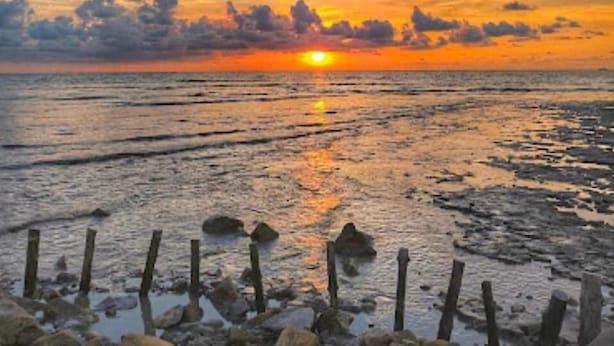 A sunset over a beach with a wooden fence in the foreground. - Audi Guest House (George Town)