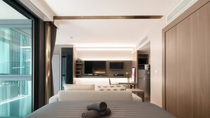 A modern hotel room with a large bed, a view of the city, a kitchenette, and a sliding door to the outside.