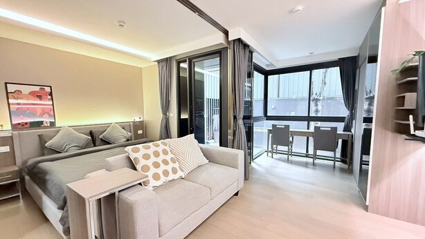 A modern hotel room with a bed, a sofa, a dining table, and a balcony with a view.