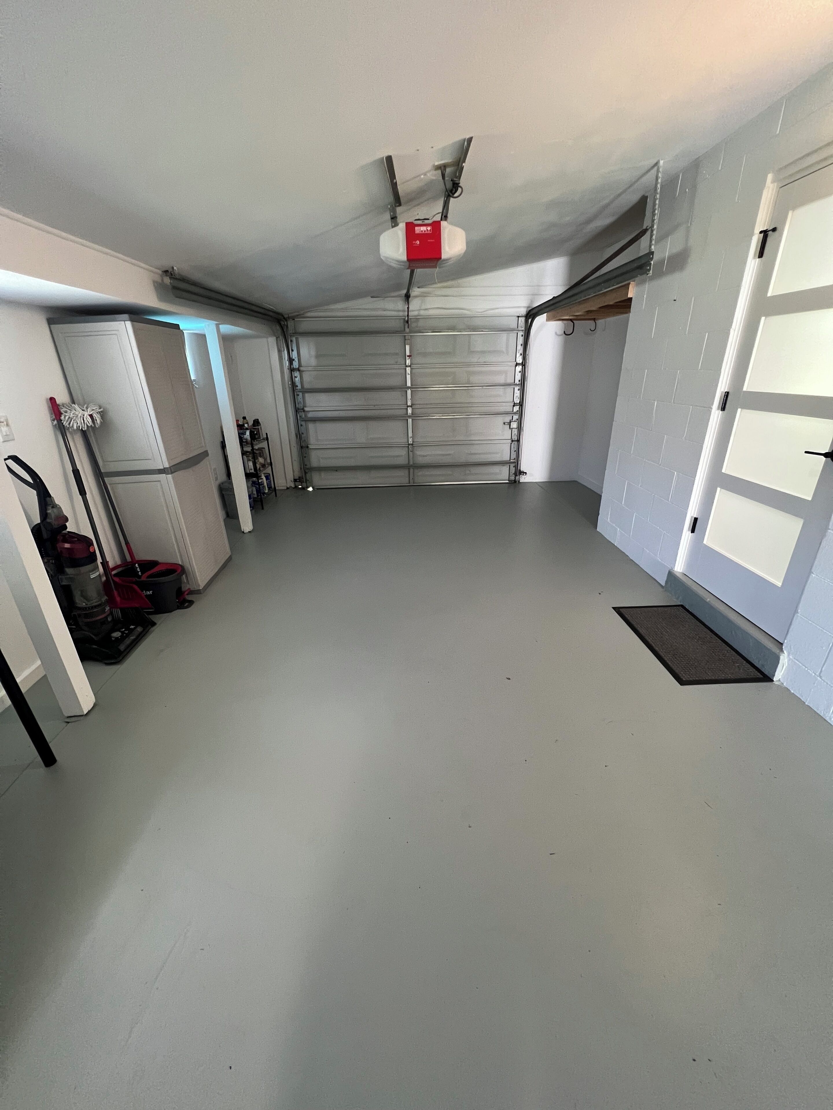 Un garaje limpio y vacío con una puerta cerrada, un ventilador de techo y un extintor rojo montado en la pared.
