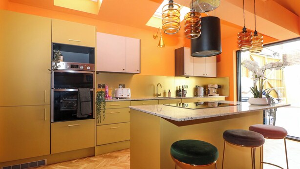 Una cocina moderna con una isla grande, electrodomésticos integrados y una decoración en tonos naranja brillante.