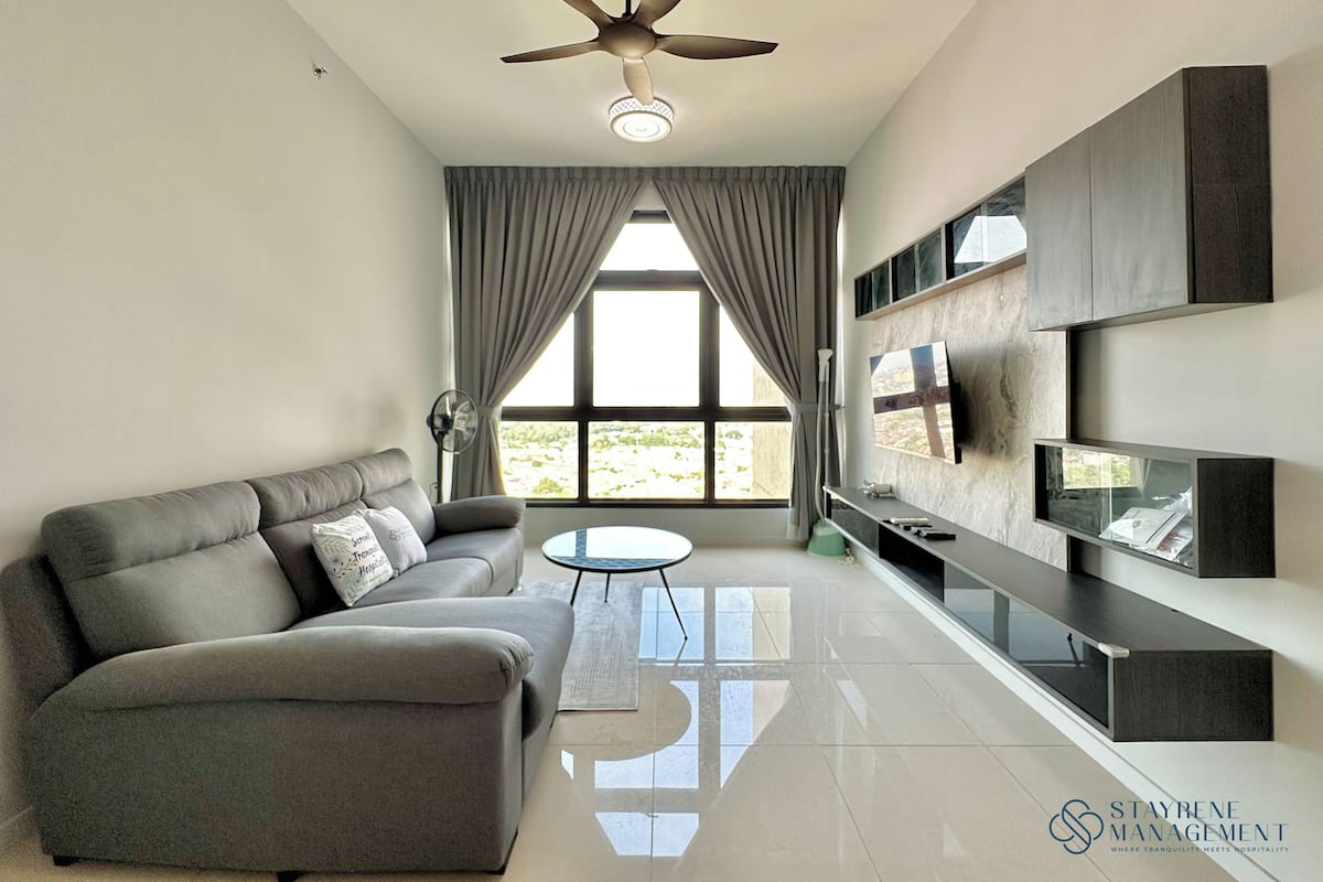 A modern living room with a sofa, a small round table, a ceiling fan, and a TV mounted on the wall.