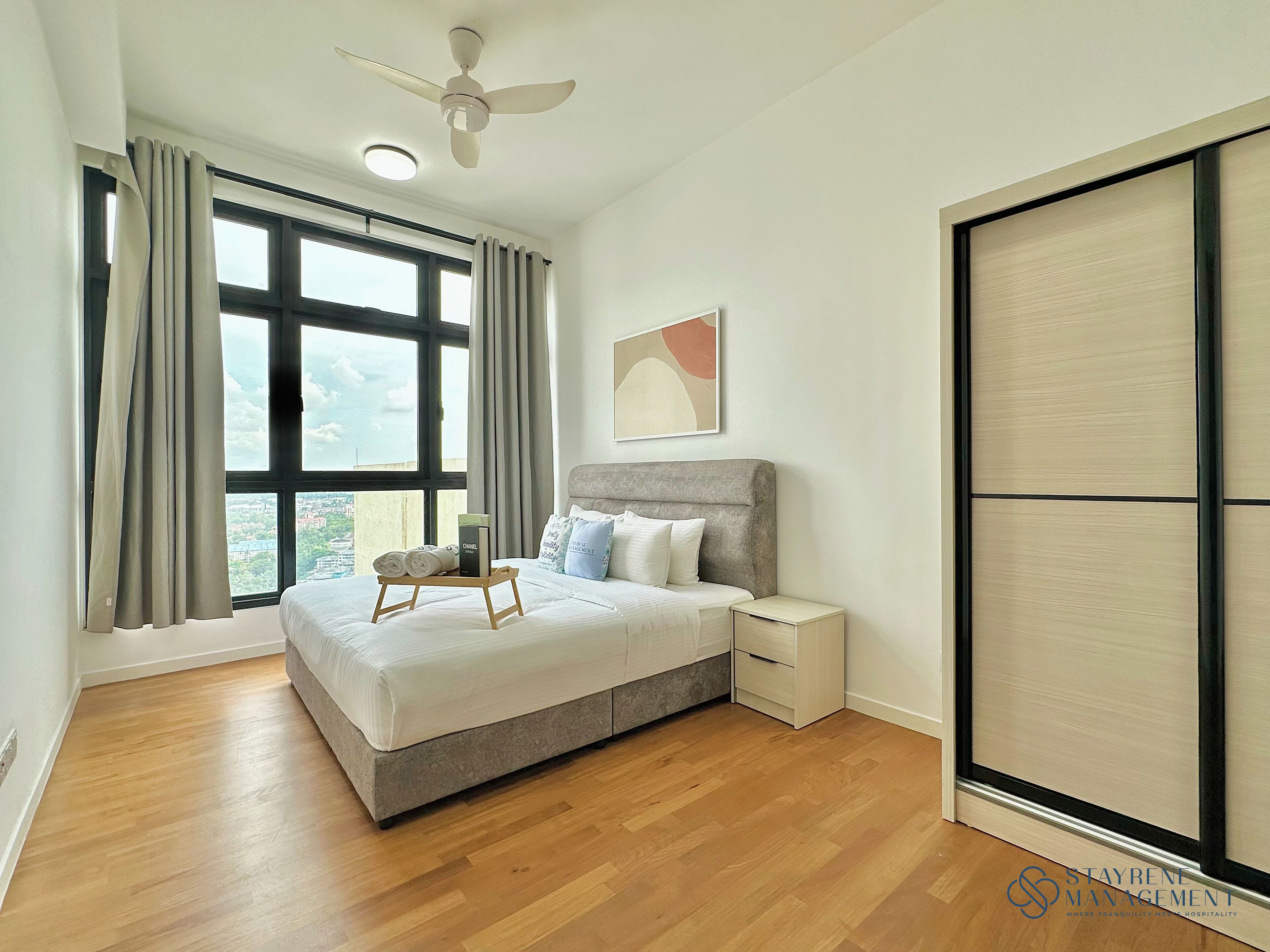 Ein Schlafzimmer mit einem Bett, einem Nachttisch, einem Deckenventilator und einem großen Fenster mit Vorhängen.