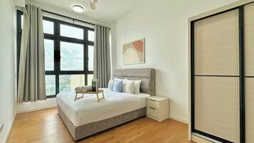 A bedroom with a bed, a bedside table, a nightstand, a ceiling fan, and a large window with curtains.